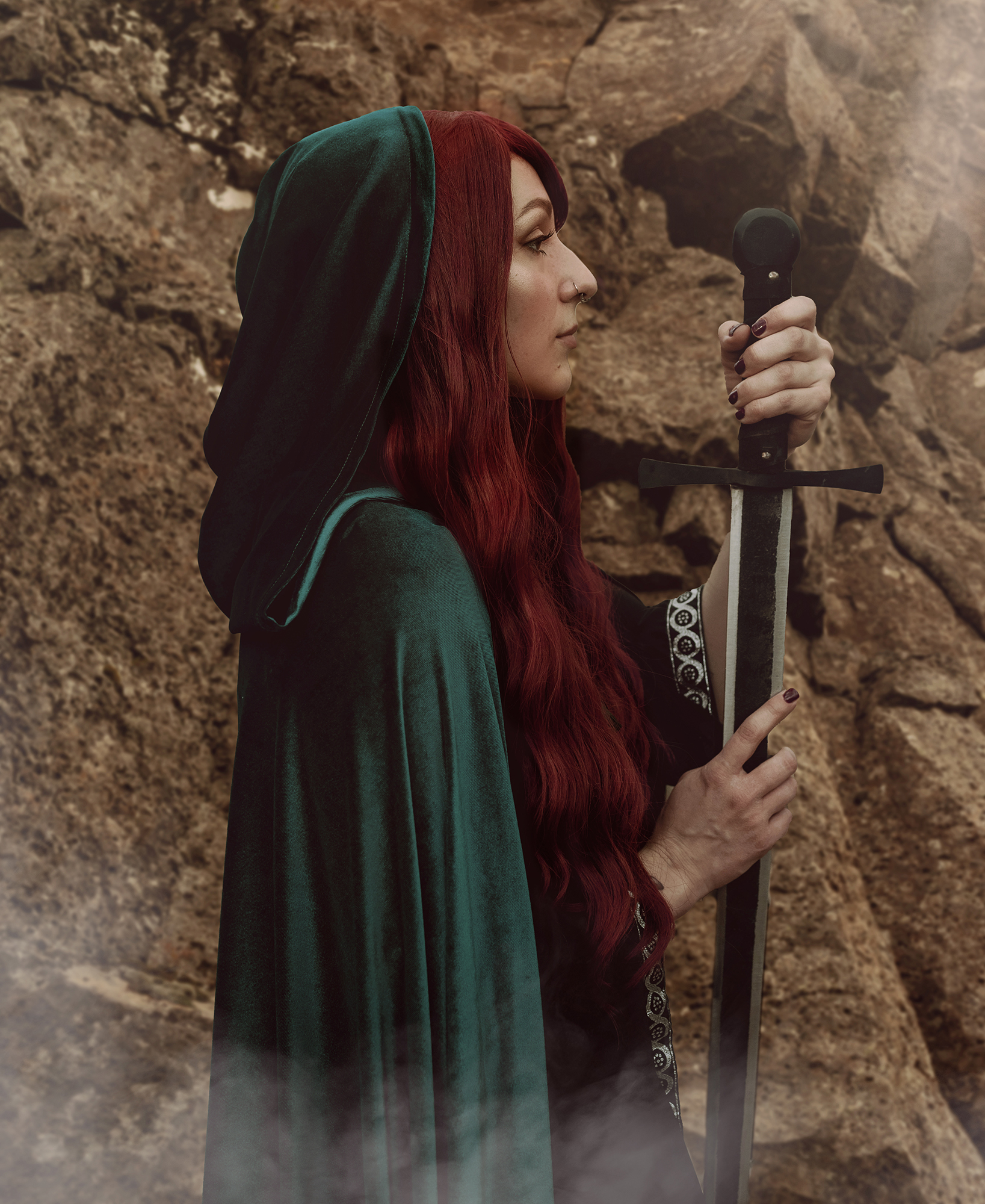 White woman with red hair wearing a fantasy costume comprised of a green velvet cape and a broad sword in Longmont Colorado for a fantasy photo shoot by Kendra Colleen Photography