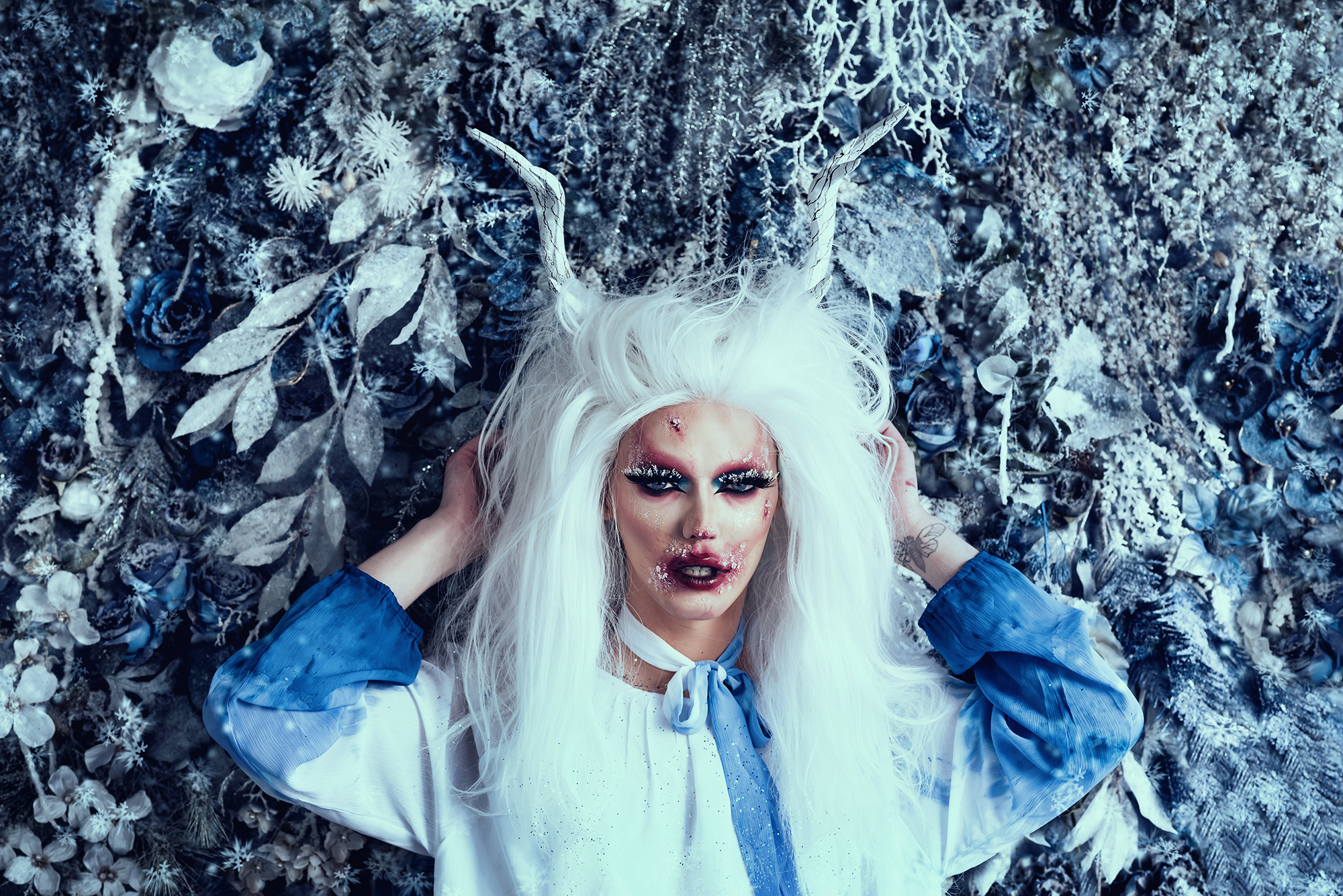 A model with white hair, elaborate makeup and fake antlers poses for a fantasy photo by Kendra Colleen Photography in Denver Colorado. 