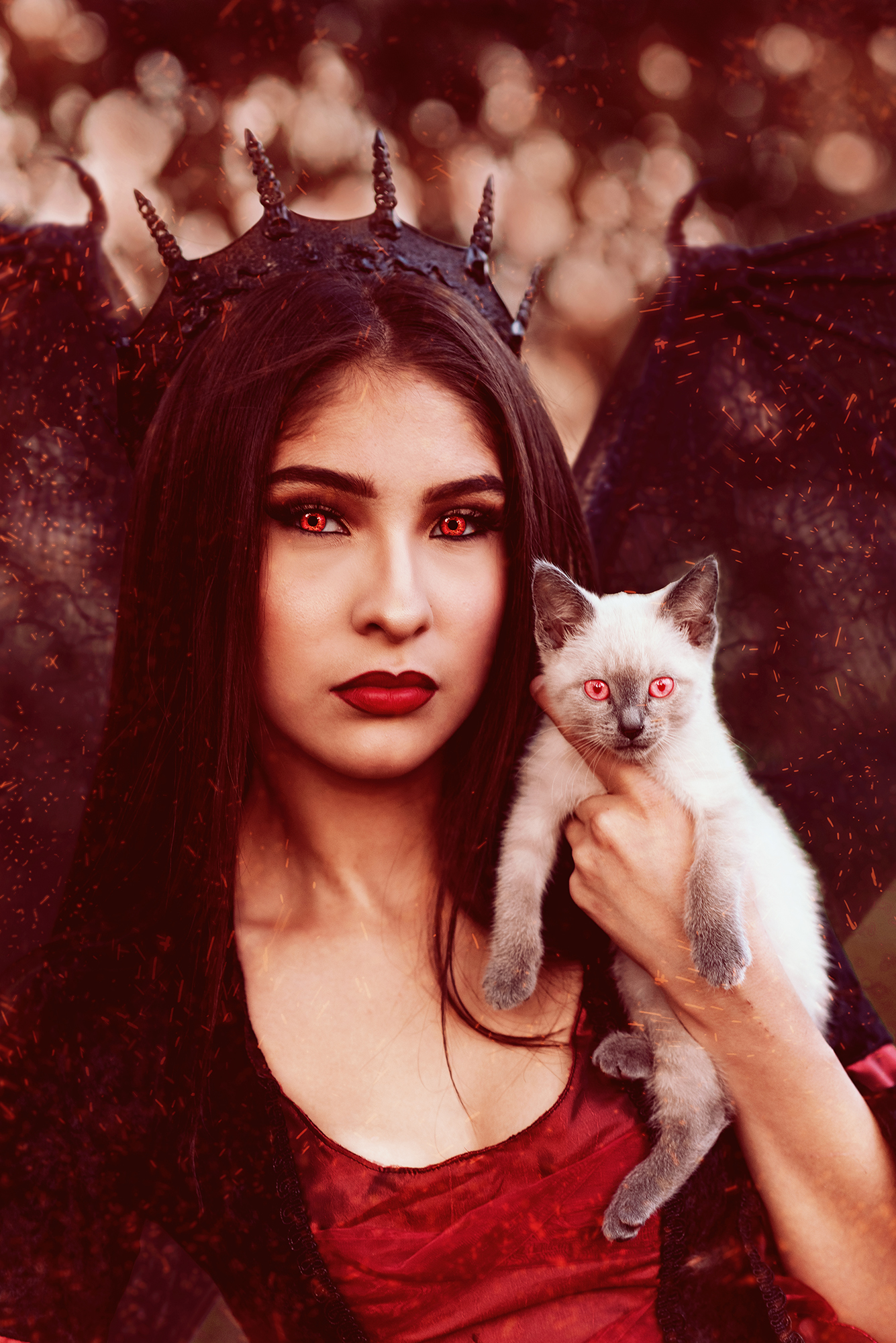 A girl dressed as a demon princess with red eyes and a black crown holds a white and gray kitten with similar red eyes for a fantasy photo shoot by Kendra Colleen Photography in Denver Colorado