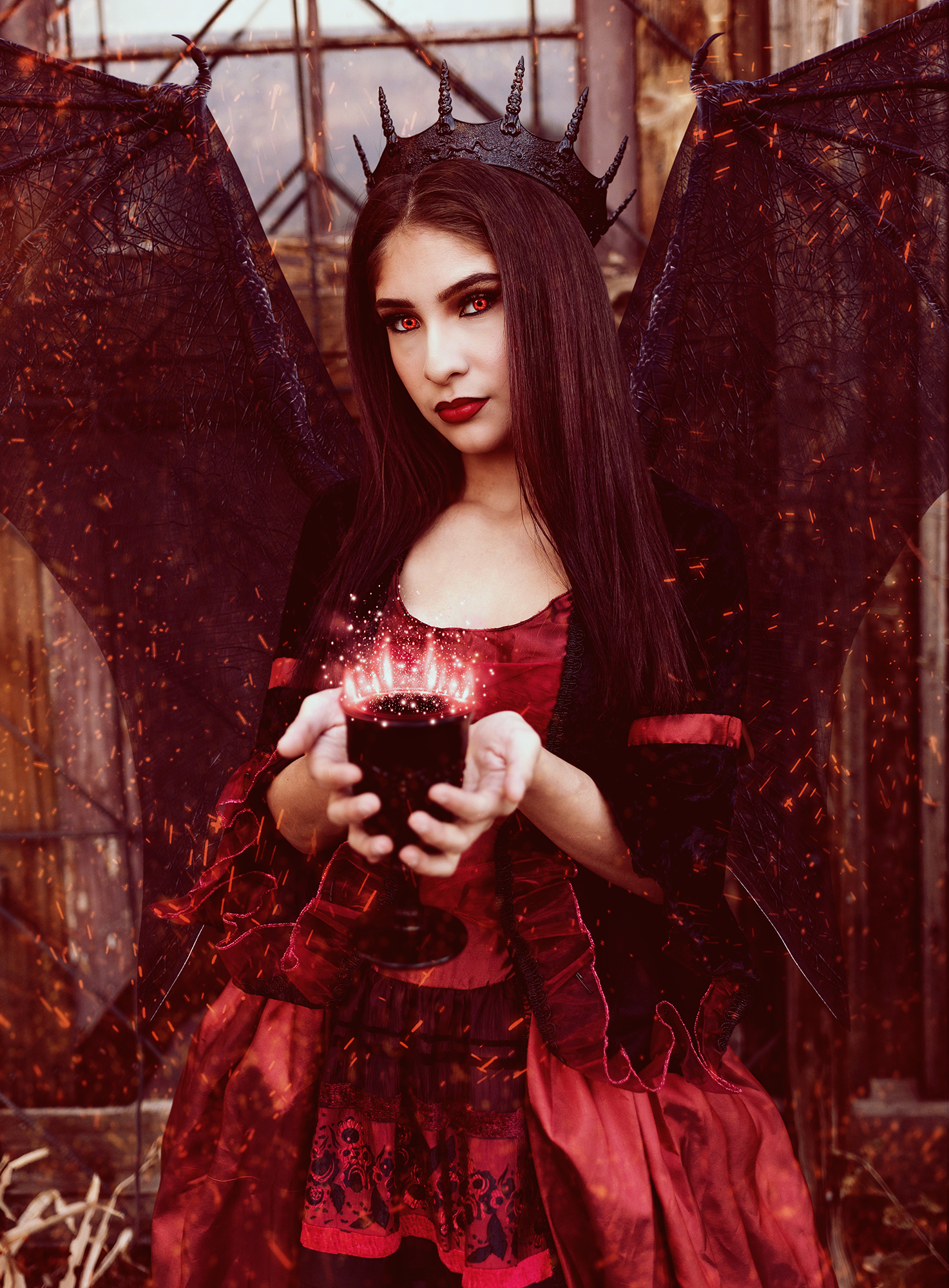 A girl dressed as a demonic princess with black wings holds a black chalice with red magic glowing around the rim for a fantasy photo shoot in Denver Colorado.