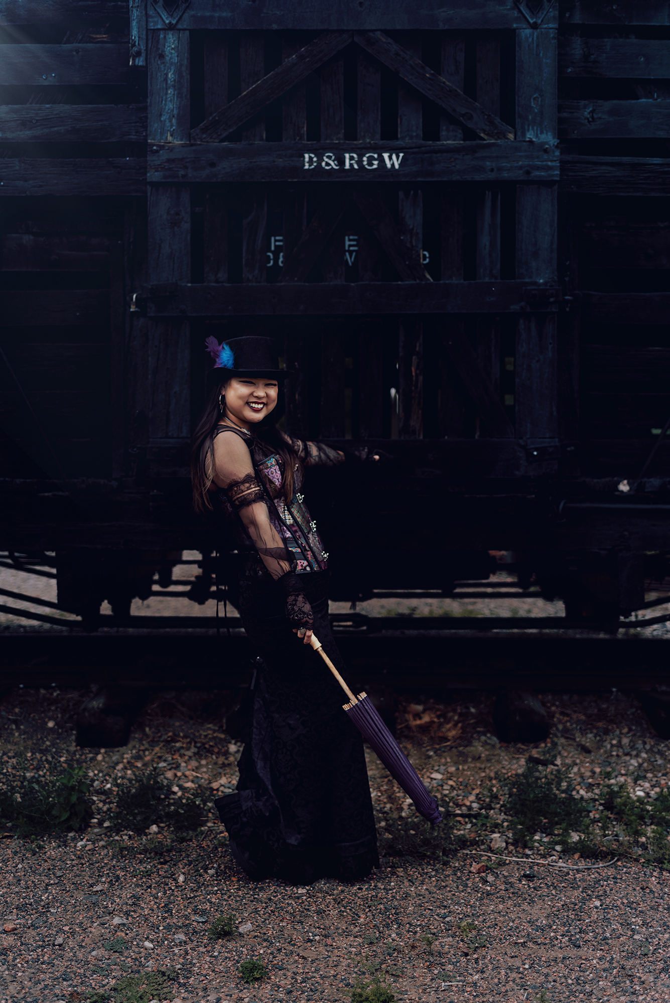 Kendra Colleen Photography takes a fantasy photo of a woman standing next to a wooden train car in a Victorian style steampunk outfit