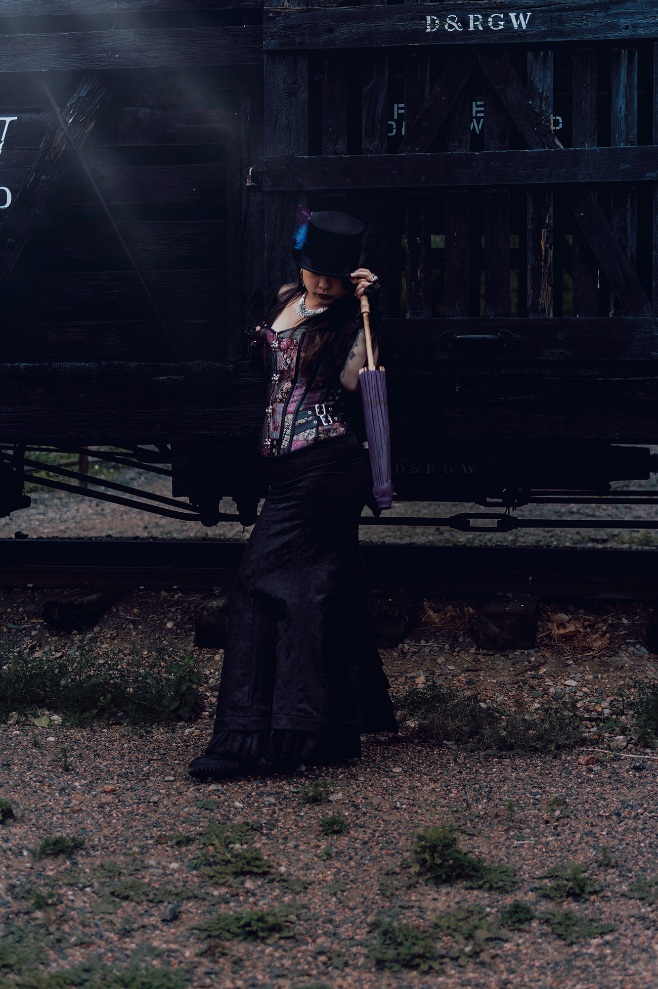 A woman standing next to a train wearing a Victorian style steampunk outfit for a fantasy photo by Kendra Colleen Photography