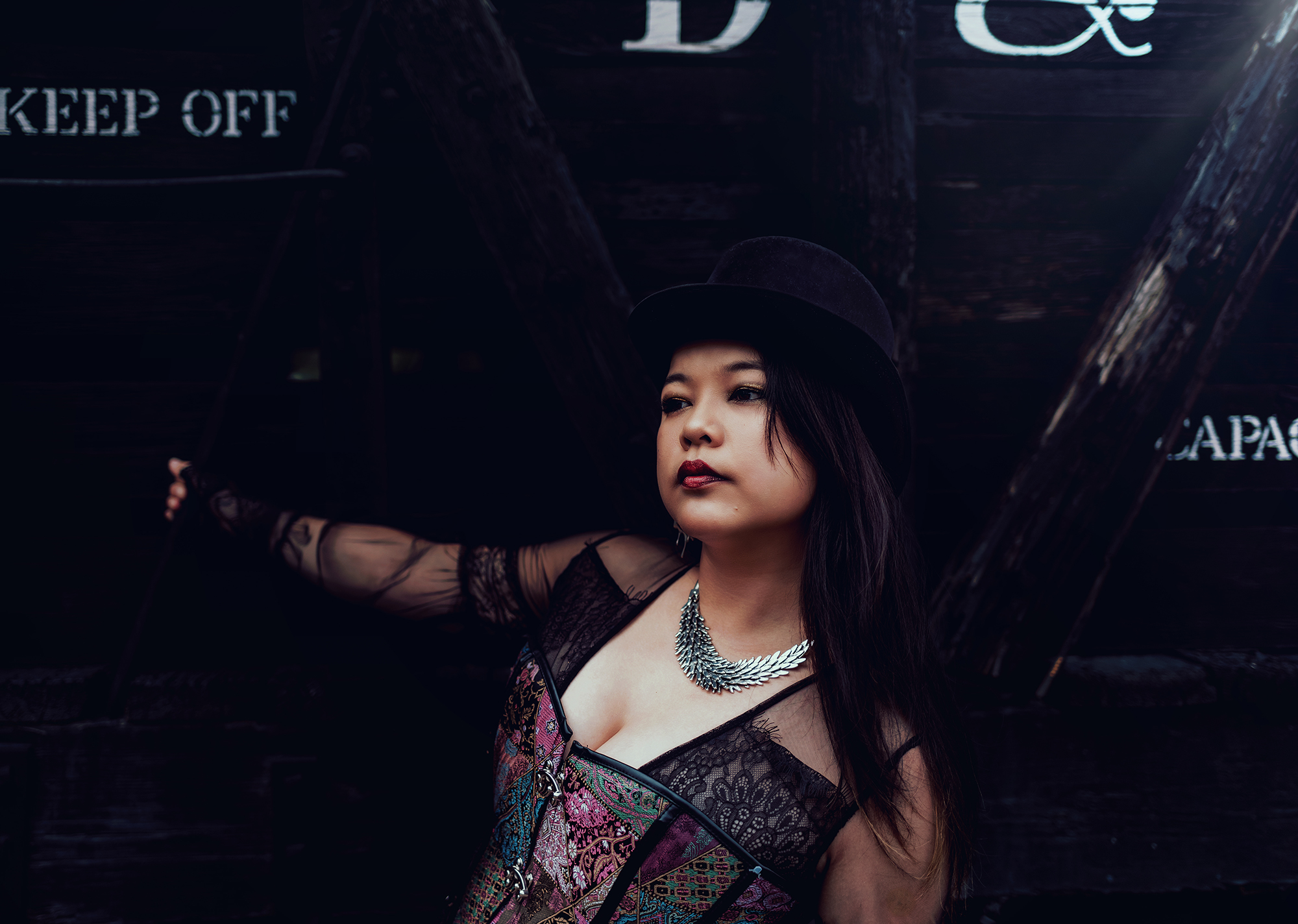 A woman wearing a top hat and colorful corset with a lace top underneath as she holds onto a train car