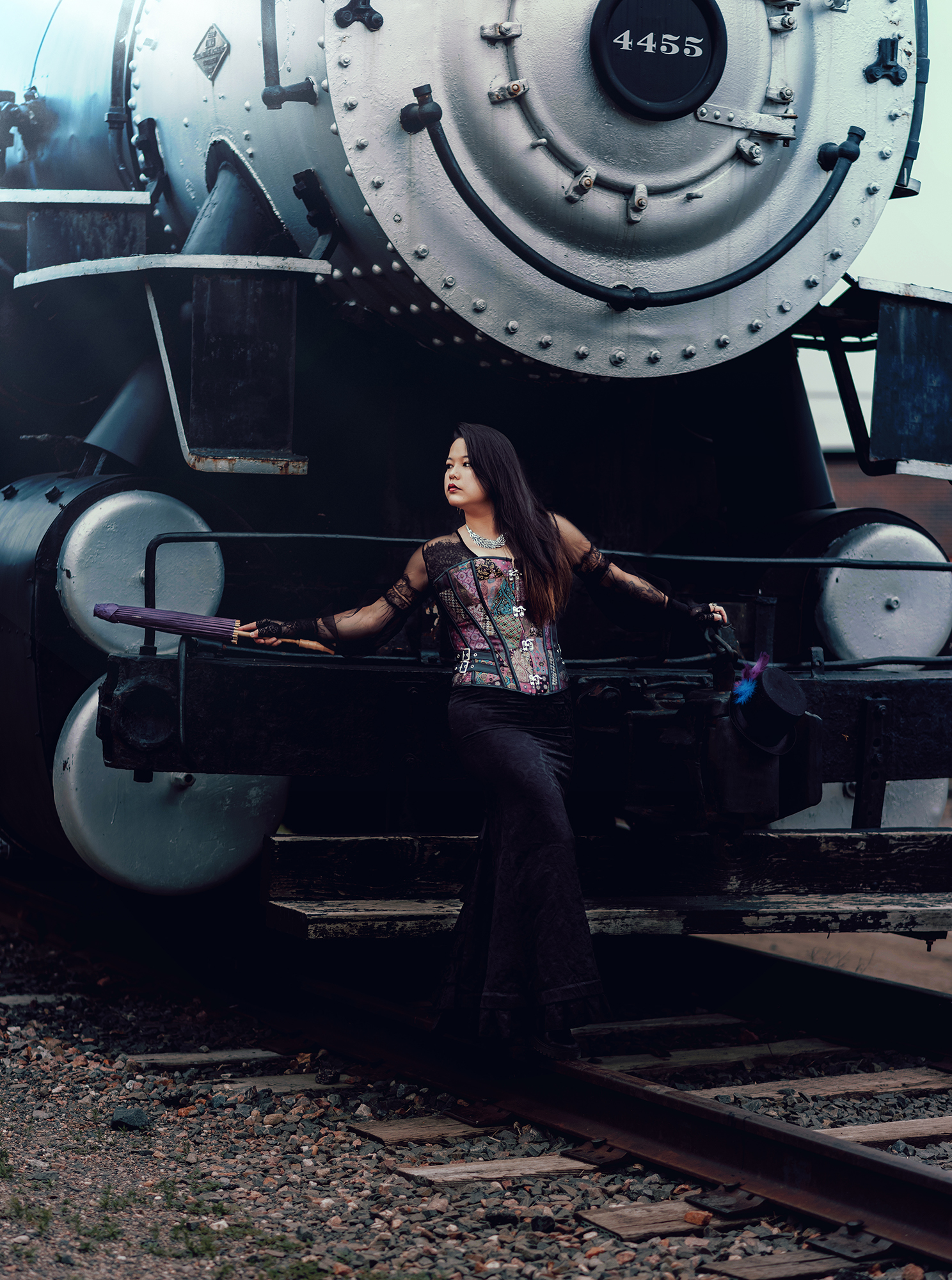 Cosplay photo by Kendra Colleen Photography of a woman standing in front of a steam engine train dressed in a Victorian style steampunk outfit.