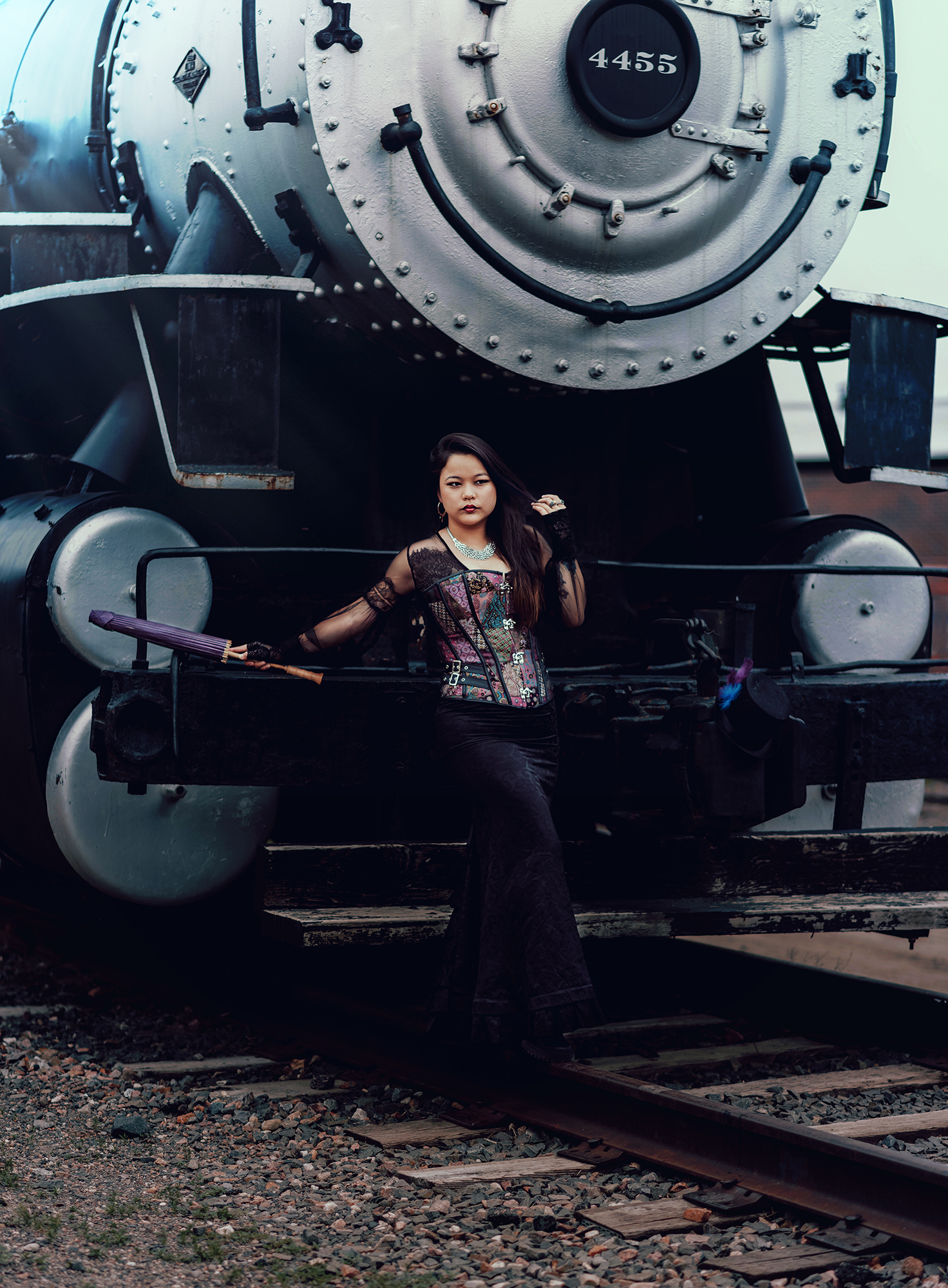 A woman stands in front of a steam engine train dressed in a Victorian steampunk style outfit for fantasy photo by Kendra Colleen Photography